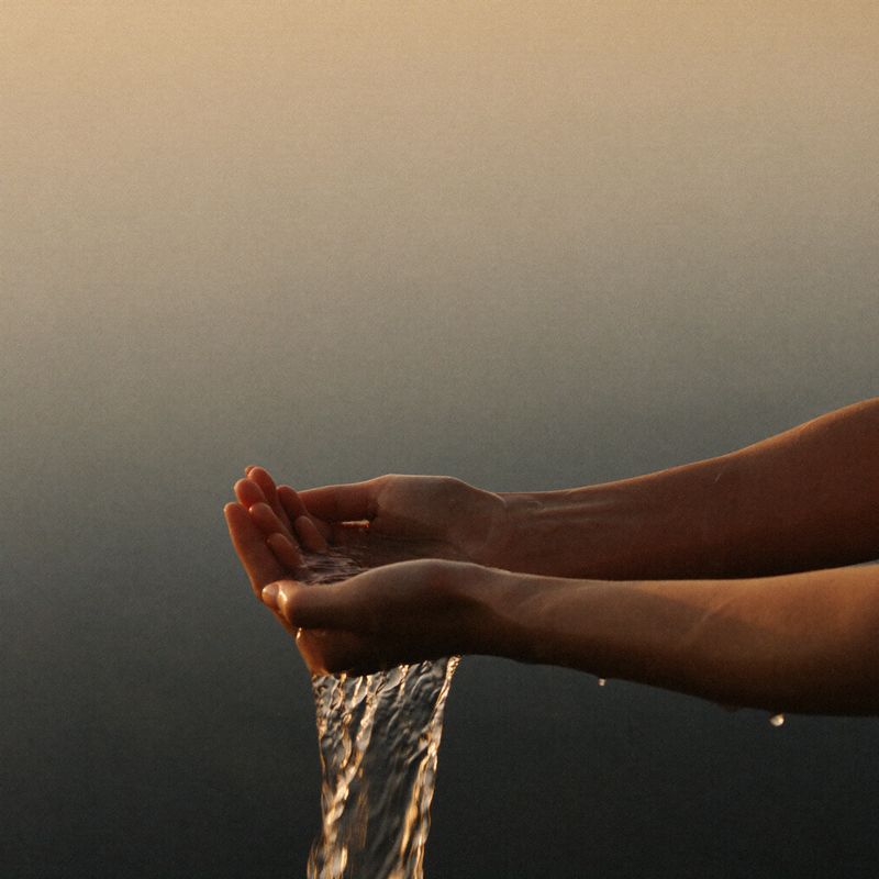 Two hands cupping golden water between them