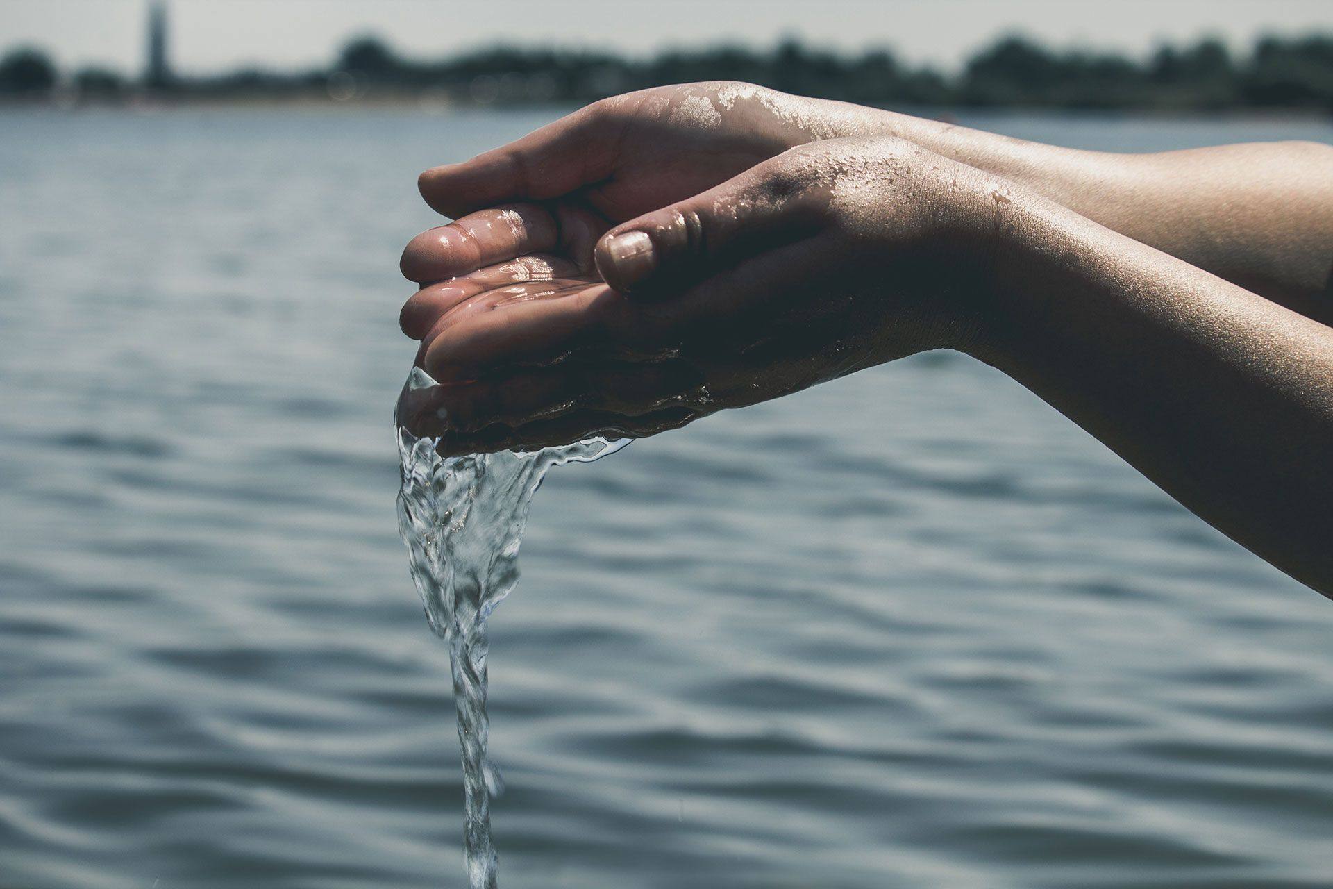 Cupped hands lifting water from a still lake, water falling through the fingers